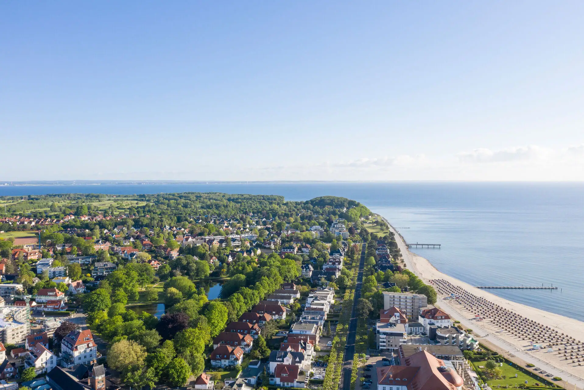Küste Travemünde Luftaufnahme einer Stadt am Wasser mit Gebäuden und Bäumen im Vordergrund.