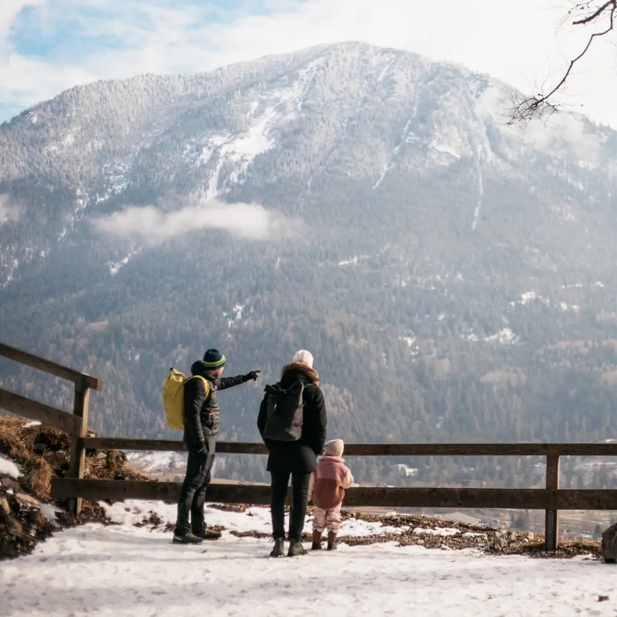 Eine Gruppe von Menschen steht auf einem verschneiten Hügel mit Blick auf ein Bergpanorama.