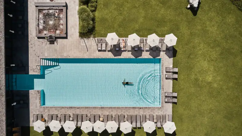 Schwimmbecken mit Sonnenschirmen und Rasen.