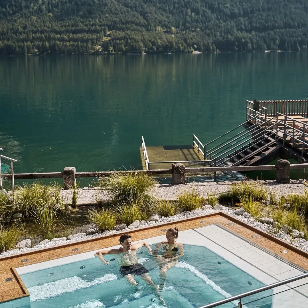 Menschen in einem Schwimmbecken mit einem Gewässer und Bergen im Hintergrund