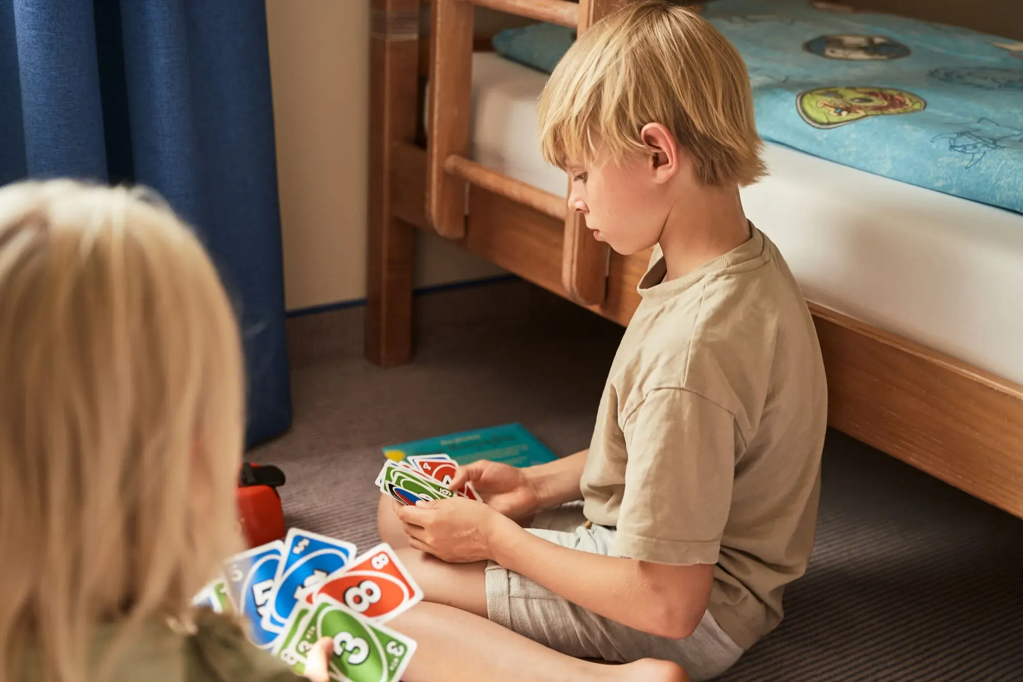 A boy and a girl are sitting on the carpet in a children's room playing the card game Uno.