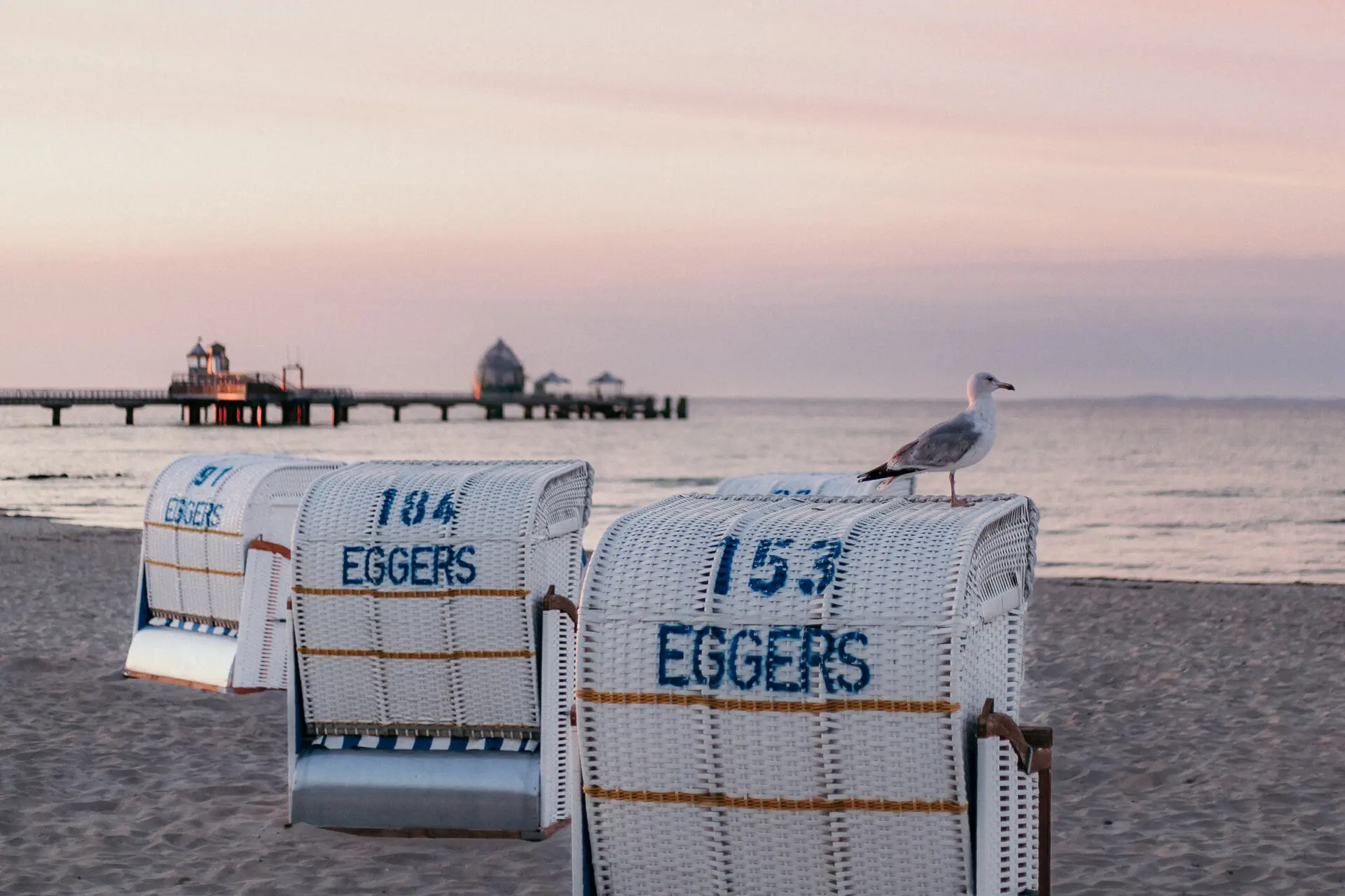 Strandkörbe stehen an einem ruhigen Strand bei Sonnenuntergang. 