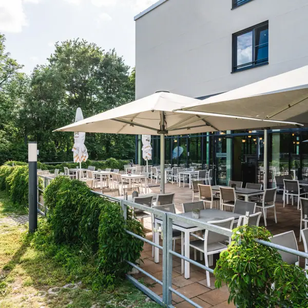 Terrasse mit Tischen und Sonnenschirmen vor einem Gebäude