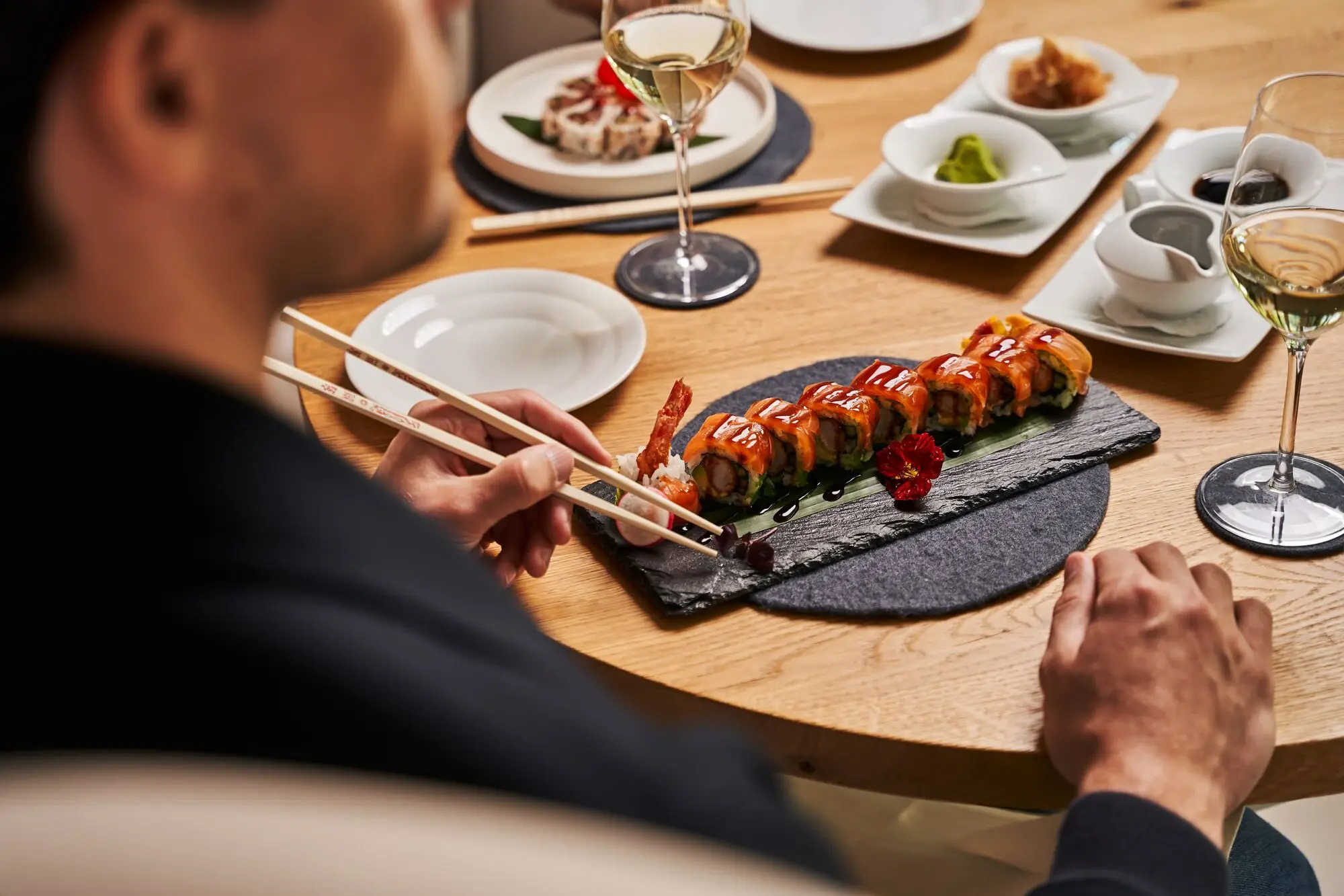 Person isst Sushi mit Stäbchen an einem Tisch.