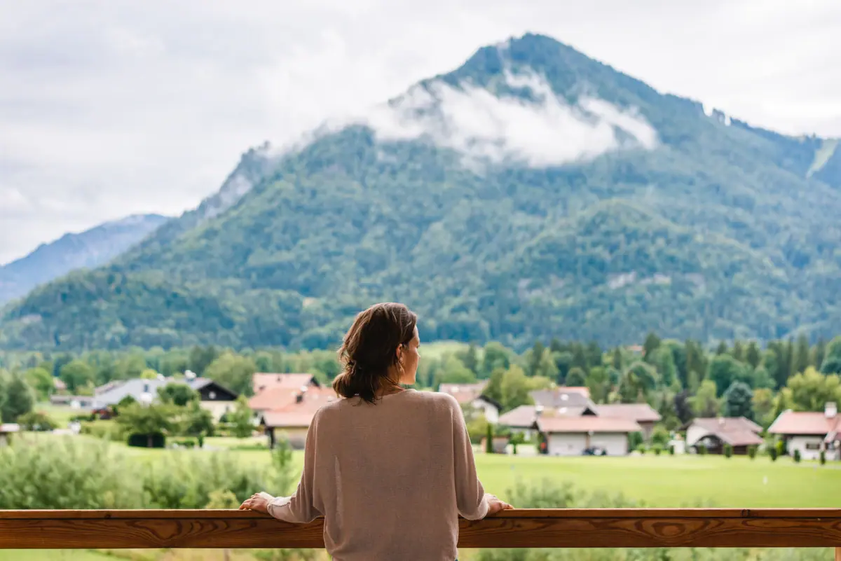 Eine Frau steht auf einem Balkon und blickt auf eine Bergkette.
