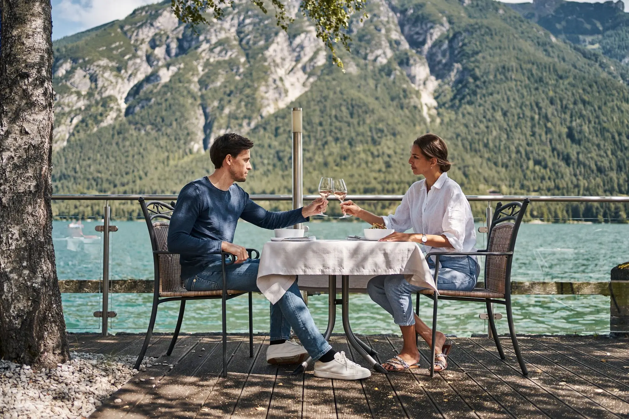 Ein Mann und eine Frau sitzen an einem Tisch und stoßen mit Weingläser an, direkt am Achensee.