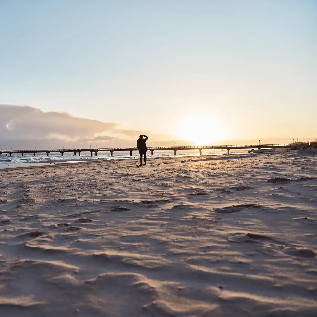 Strand Eine Person geht am Strand entlang unter einem bewölkten Himmel.
