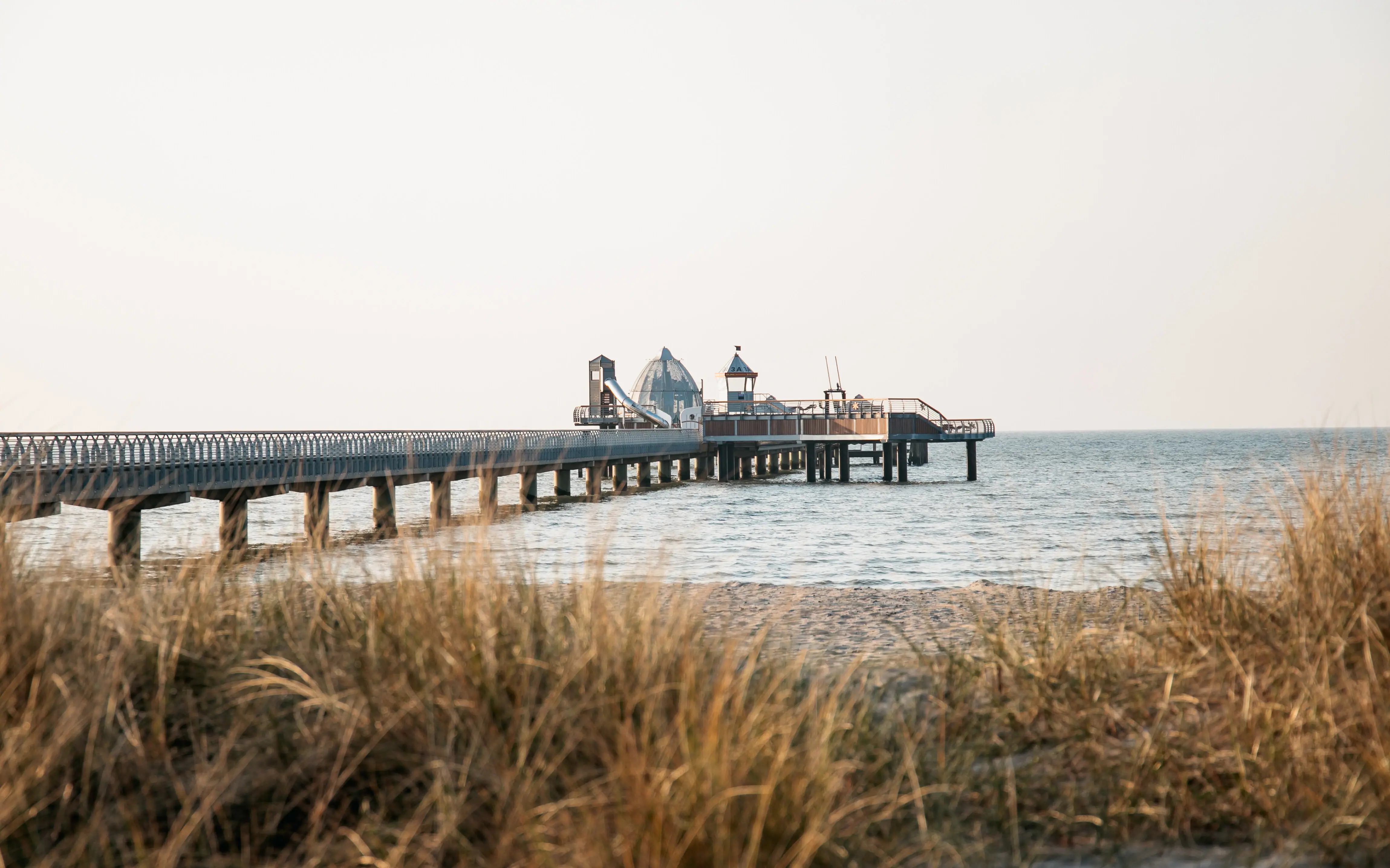 Ein langer Pier mit Strand und Gras im Vordergrund.