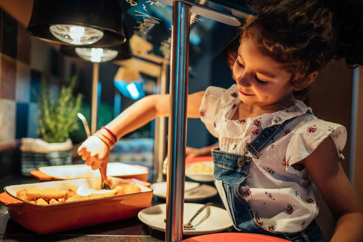 Mädchen in Latzhose und weißem Hemd steht am aja Kinder Buffet.