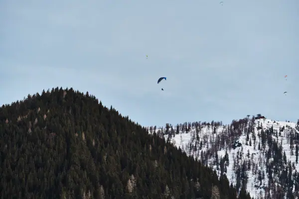 Eine Gruppe von Menschen beim Fallschirmspringen am Himmel über einem Berg.