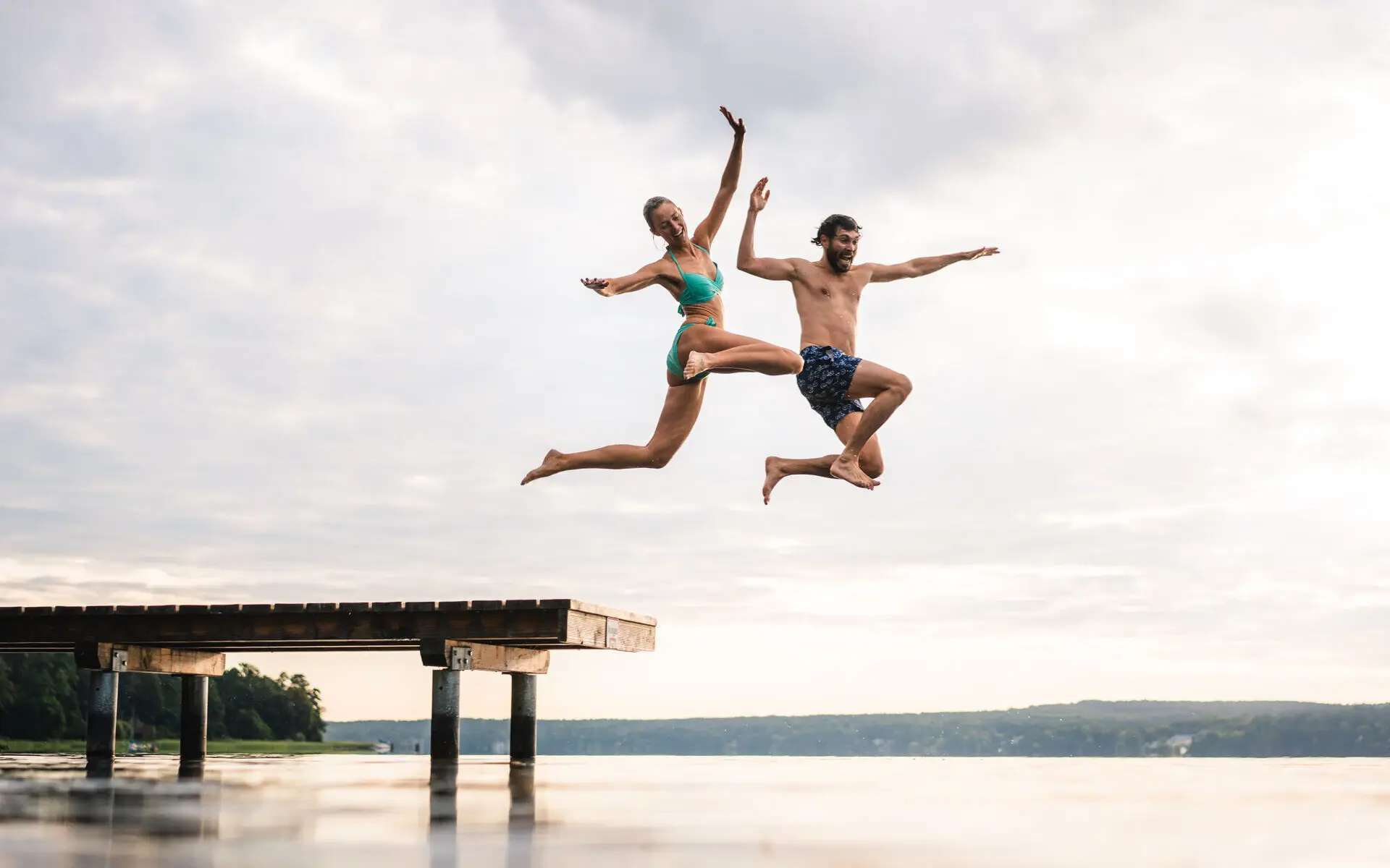 Ein Mann und eine Frau springen in einen See von einem Steg.