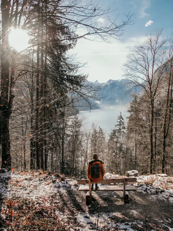 Eine Person sitzt auf einer Bank mit Blick auf einen See in einer winterlichen Landschaft.