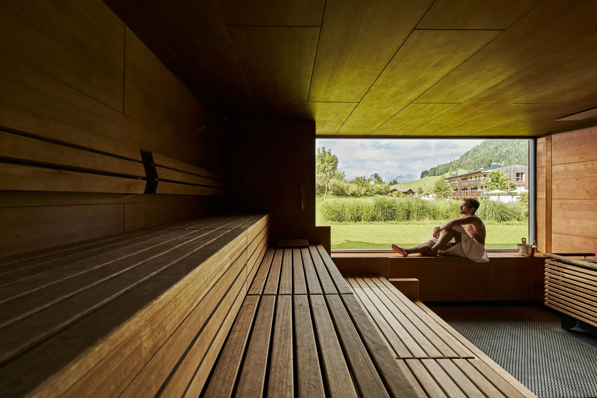 Mann sitzt auf einer Bank in einer Sauna mit Fenster.