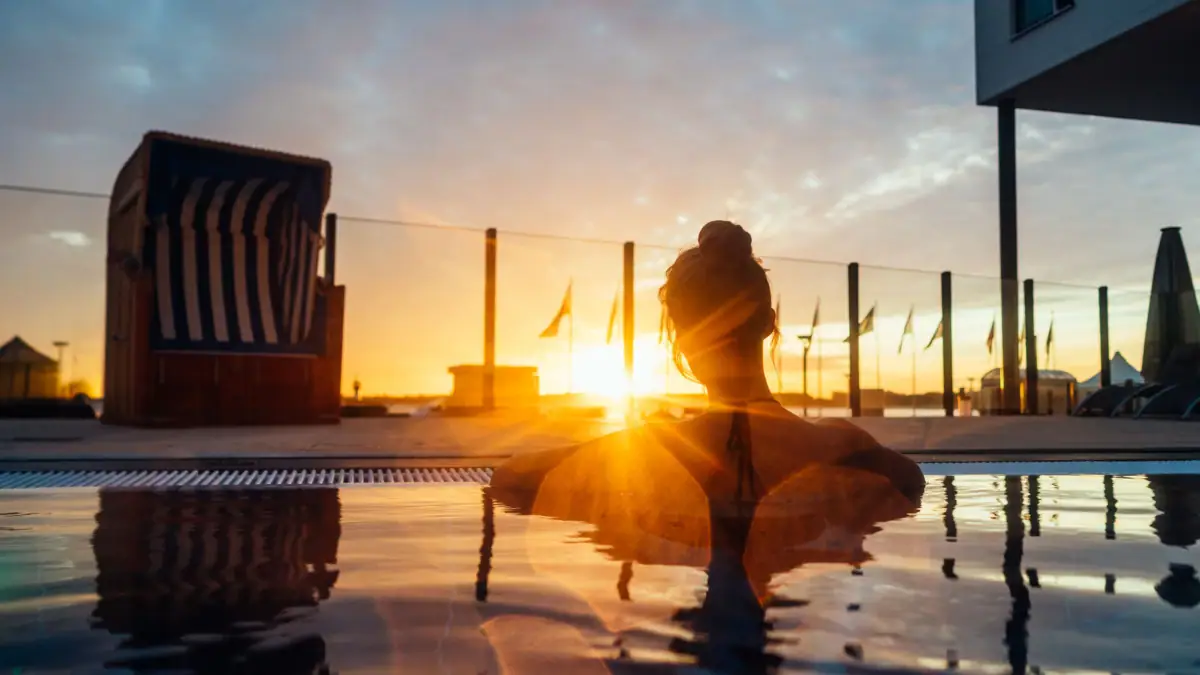 Außenpool aja Travemünde Eine Frau sitzt in einem Pool mit Sonnenuntergang im Hintergrund.