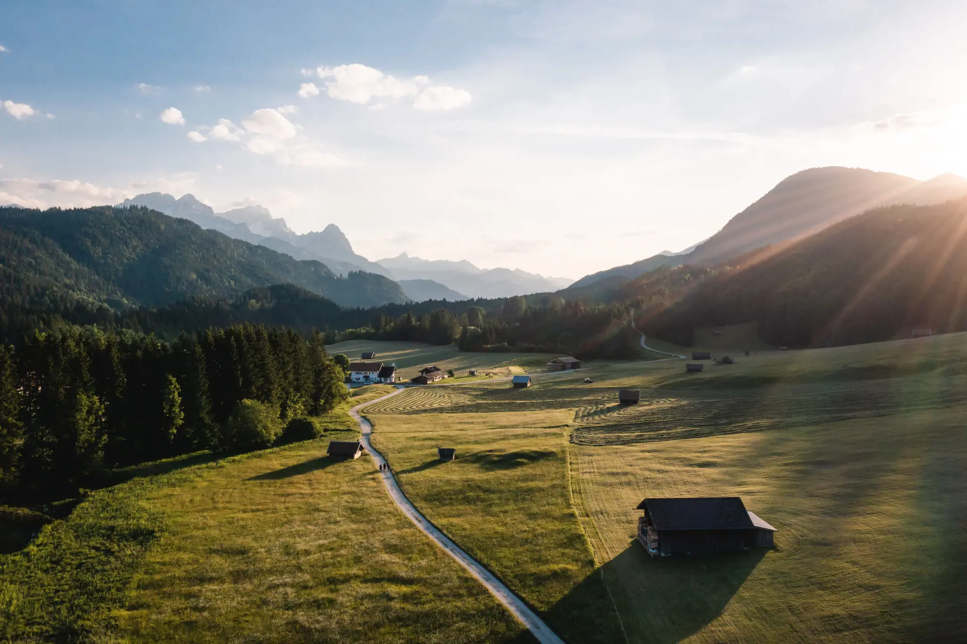 Ein grünes Tal in den bayrischen Alpen, durch das eine Straße mit eijn paar Häusern führt. 