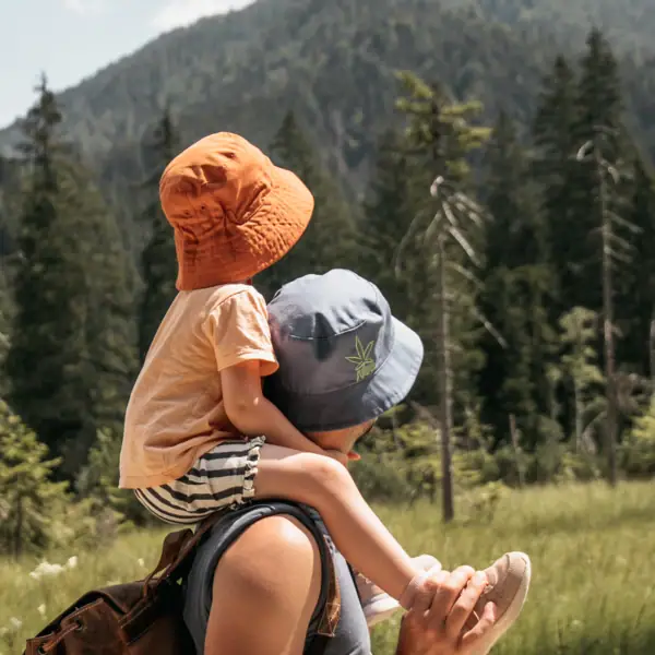 Ein Mann trägt ein Kind auf seinen Schultern in einem Feld mit Bäumen und Bergen.