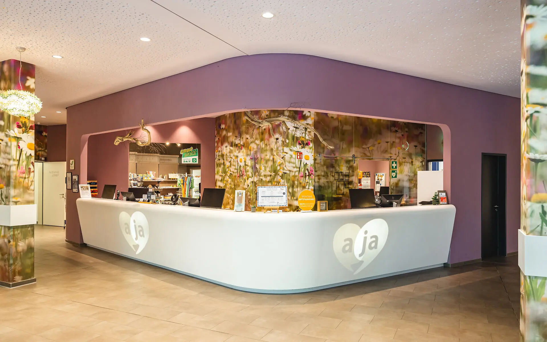 Ansicht der aja Bad Saarow Lobby mit naturnahen Blumentapeten und lilafarbener Wandfarbe. 