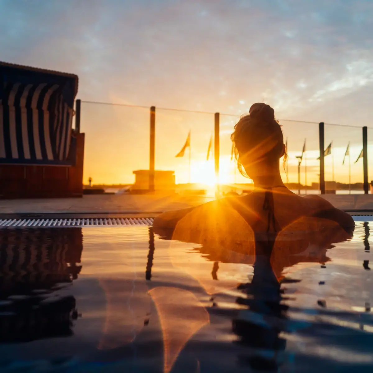 Eine Frau entspannt in einem Pool mit Sonnenuntergang im Hintergrund.