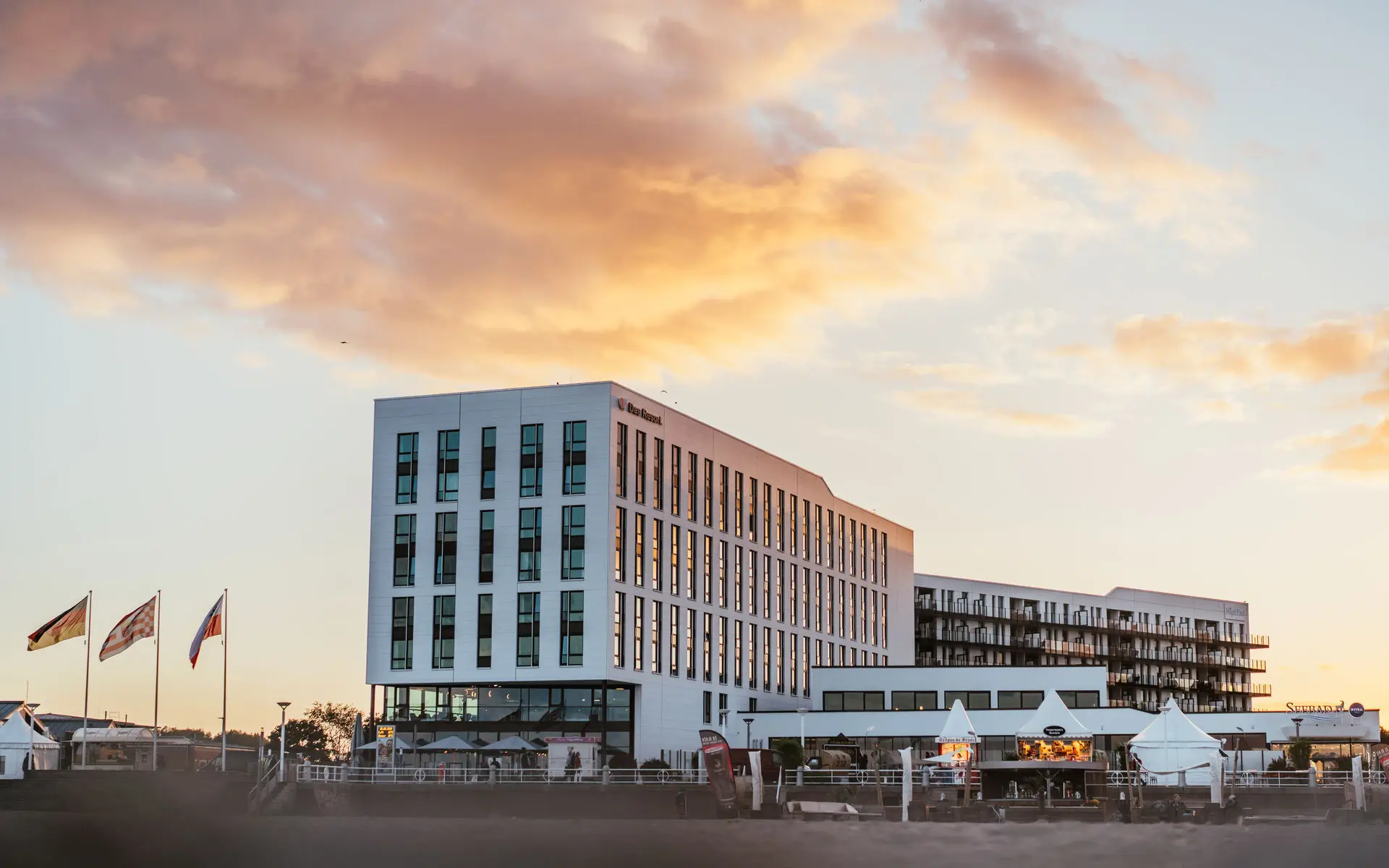 Eine Außenansicht eines weißen Gebäudes mit vielen Fenstern an einem Strand bei Sonnenuntergang. 