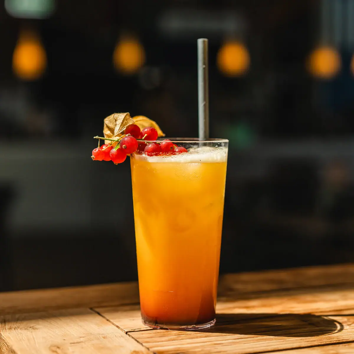 Ein Glas mit orange-gelbem Drink, Trinkhalm und Beeren.