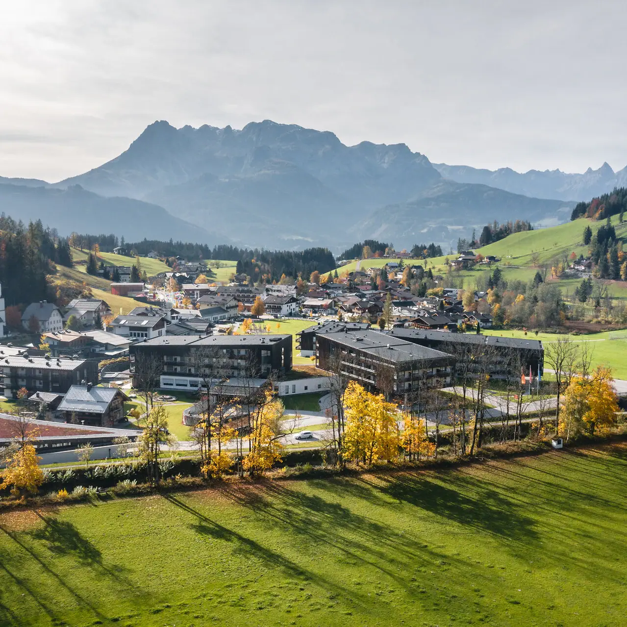 aja Bergresort Werfenweng Stadt in einem Tal mit Bergen im Hintergrund und leicht bewölktem Himmel.