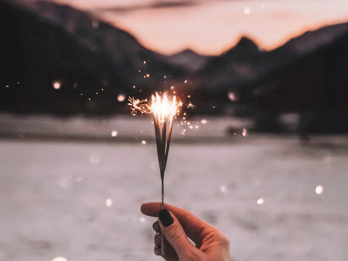 Hand hält eine Wunderkerze vor einem Himmel im Hintergrund die Berge
