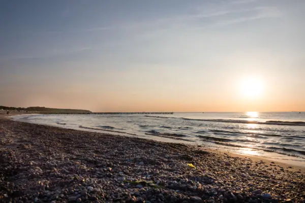 Strand mit Felsen, Wasser und einem Pier im Hintergrund.