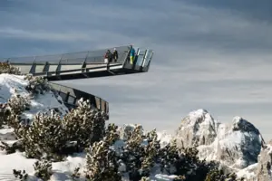 Menschen gehen auf einer Aussichtsplattform über einem verschneiten Berg.