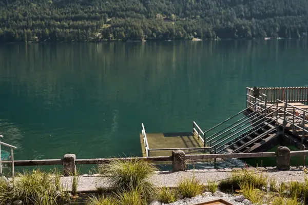Menschen in einem Pool am See mit Bergkulisse im Hintergrund.