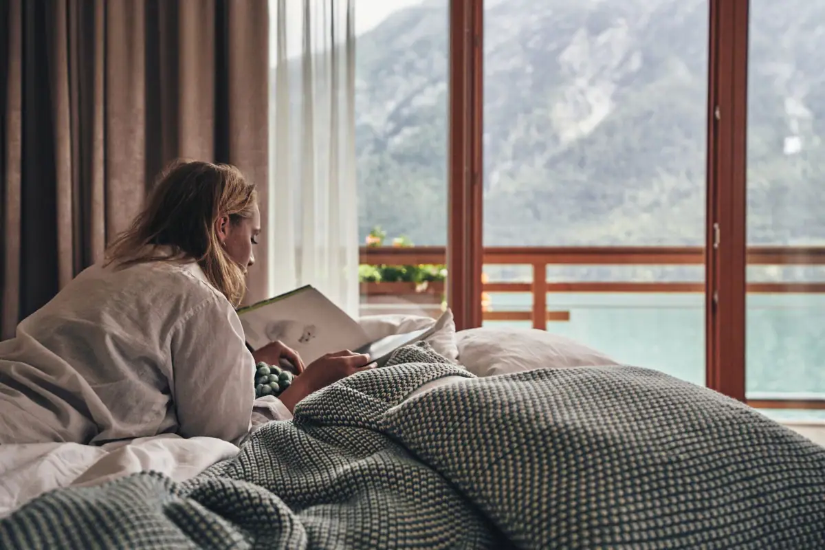 Zimmer mit Ausblick auf den Achensee Frau liegt auf einem Bett und liest ein Buch.