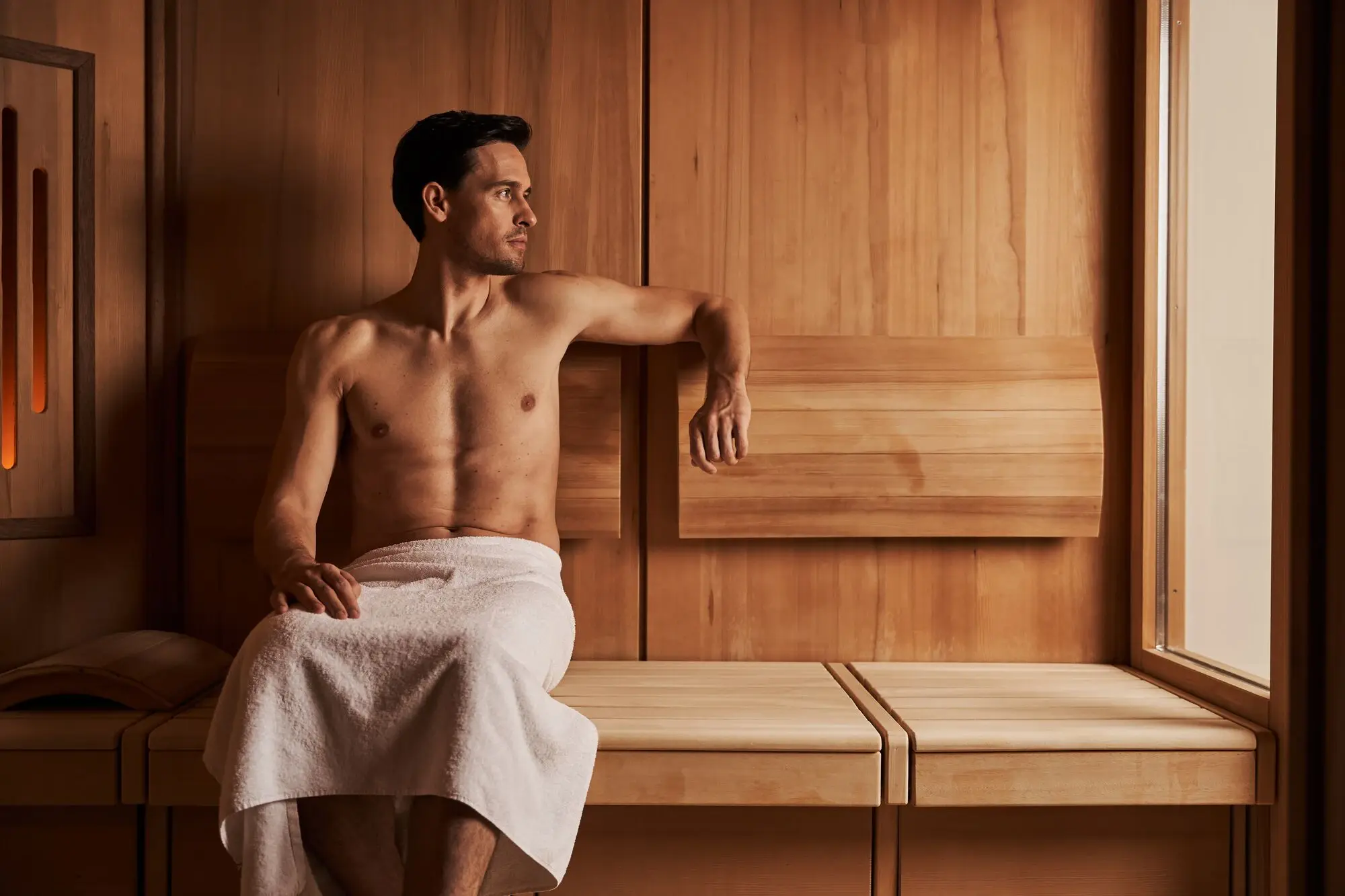 Mann sitzt in einer Sauna, mit einem Handtuch bekleidet.