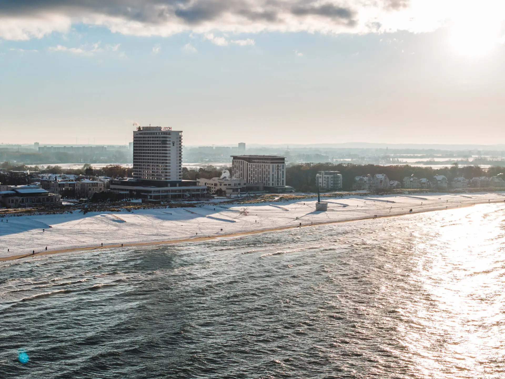 aja Warnemünde Strand mit dem aja Warnemünde und Schnee im Vordergrund, bewölkter Himmel im Hintergrund.