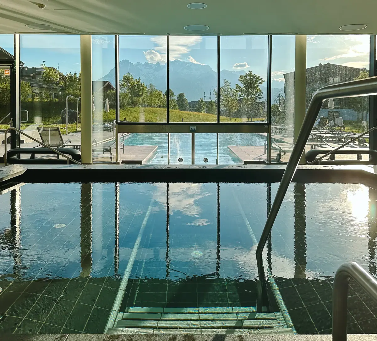Der Poolbereich im aja Bergresort Werfenweng mit Innen und Außenpool und Bergen im Hintergrund.