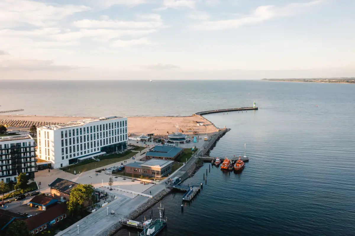 Das aja Travemünde direkt am Wasser gelegen mit Booten und Gebäuden im Hintergrund.