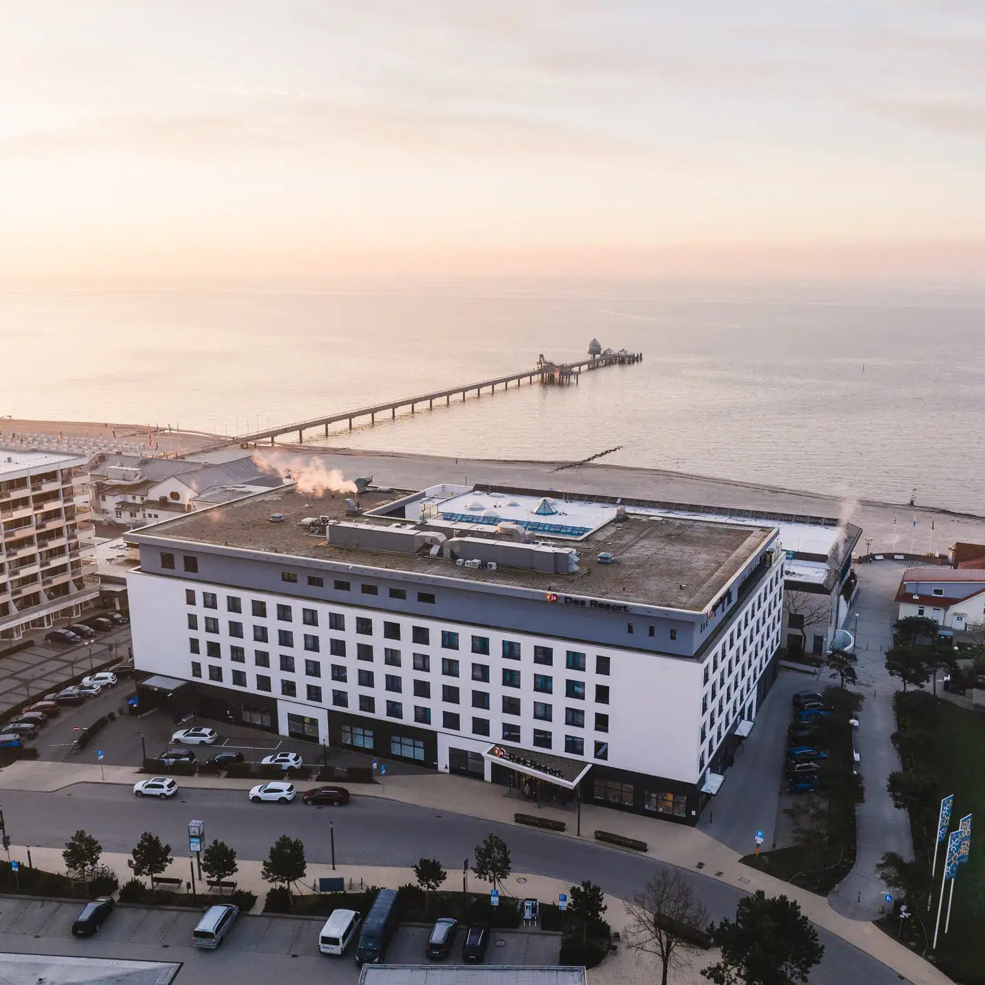 aja Grömitz Ein Gebäude neben einem Gewässer unter einem bewölkten Himmel.
