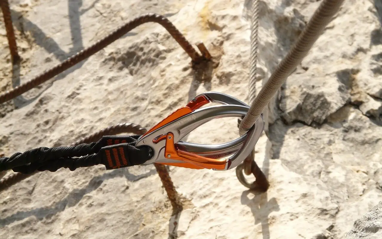 Nahaufnahme eines Karabiners, der an einem Drahseil in einem Felsen festgemacht ist.