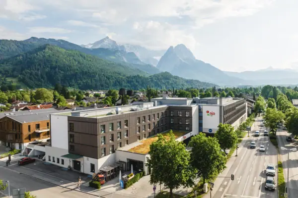 aja Hotel Garmisch-Partenkirchen Ein Gebäude mit Bäumen und Bergen im Hintergrund.