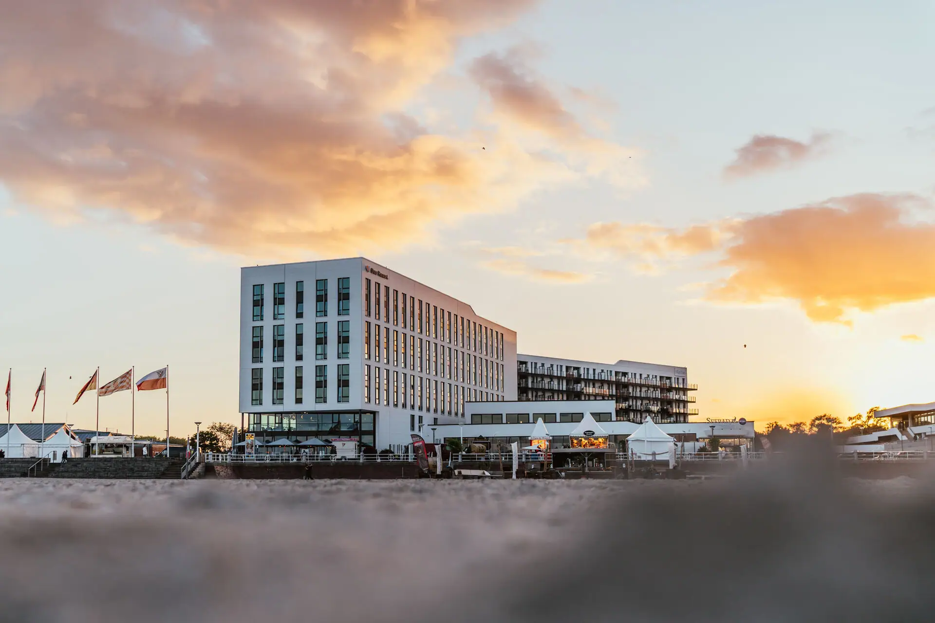 aja Travemünde Ein Gebäude mit Flaggen davor bei Sonnenaufgang.