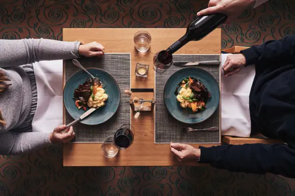 Eine Person gießt Wein über ein Gericht auf einem Teller.