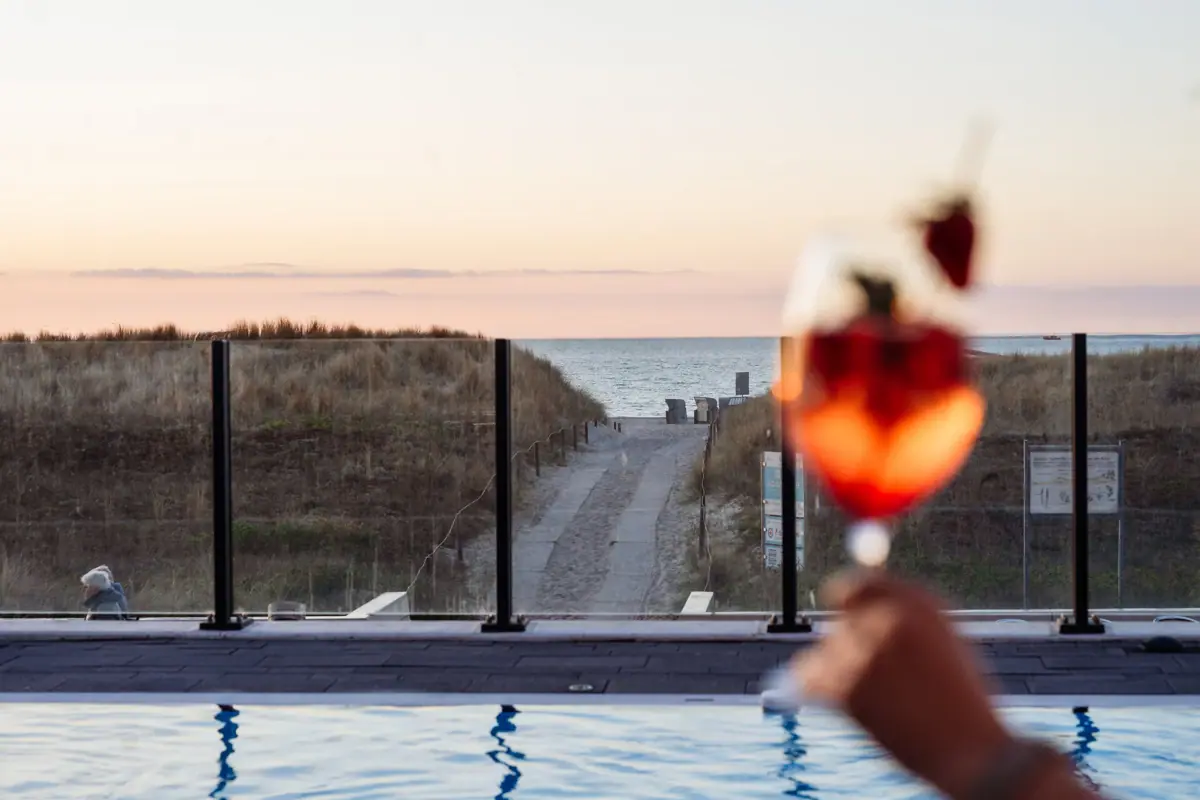 Hand hält ein Weinglas mit Erdbeeren über einem Pool.