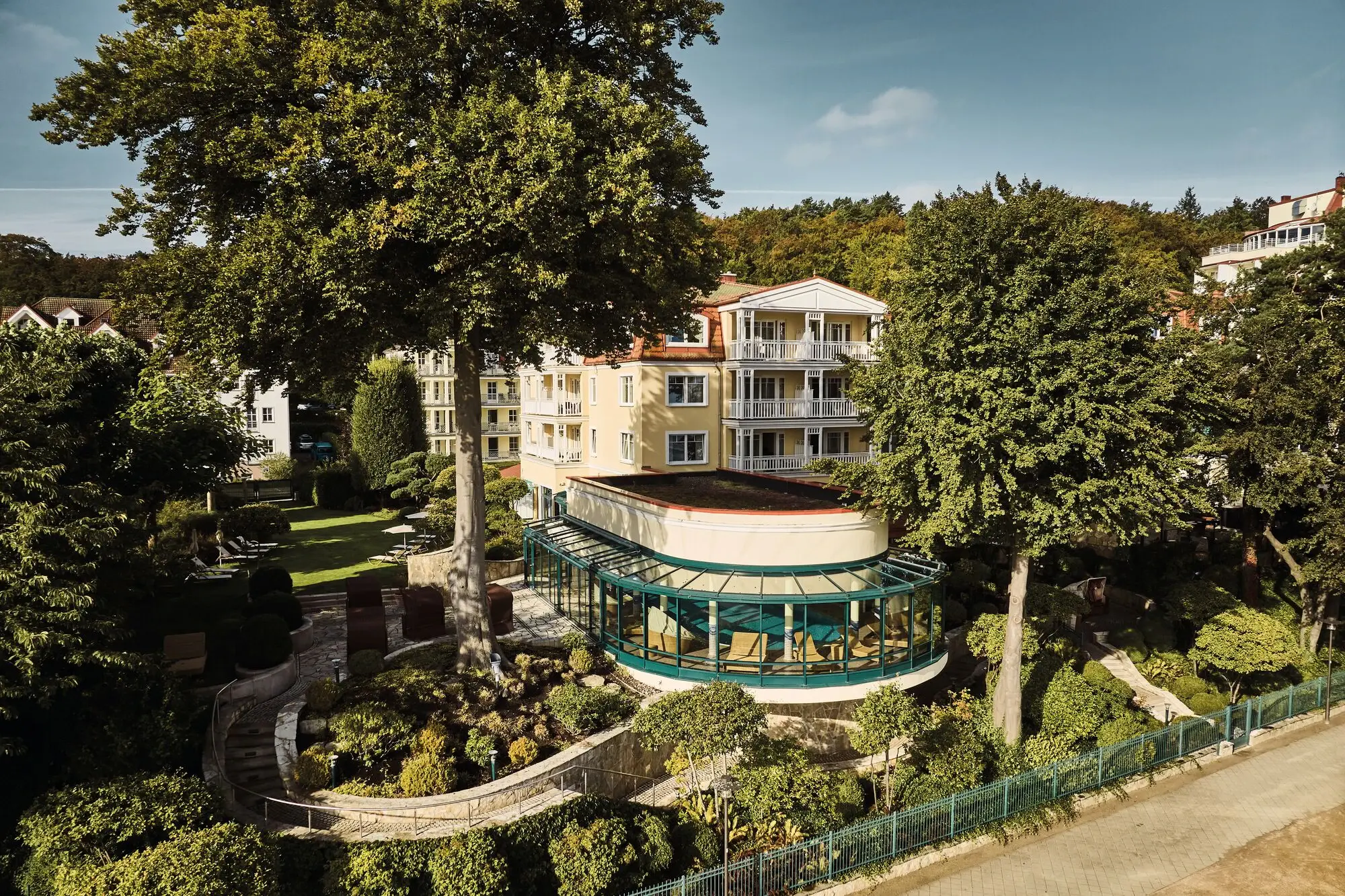 Außenansicht des Strandhotels Bansin mit verglastem Wintergarten, umgeben von altem Baumbestand und gepflegtem Garten in idyllischer Lage auf Usedom.