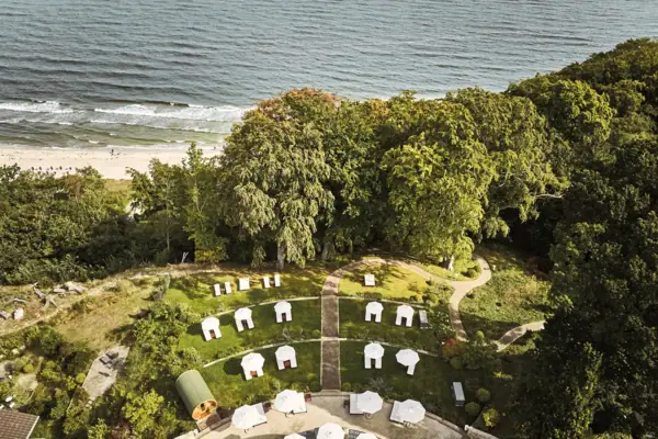Luftaufnahme eines Strandes mit weißen Zelten und Sonnenschirmen.