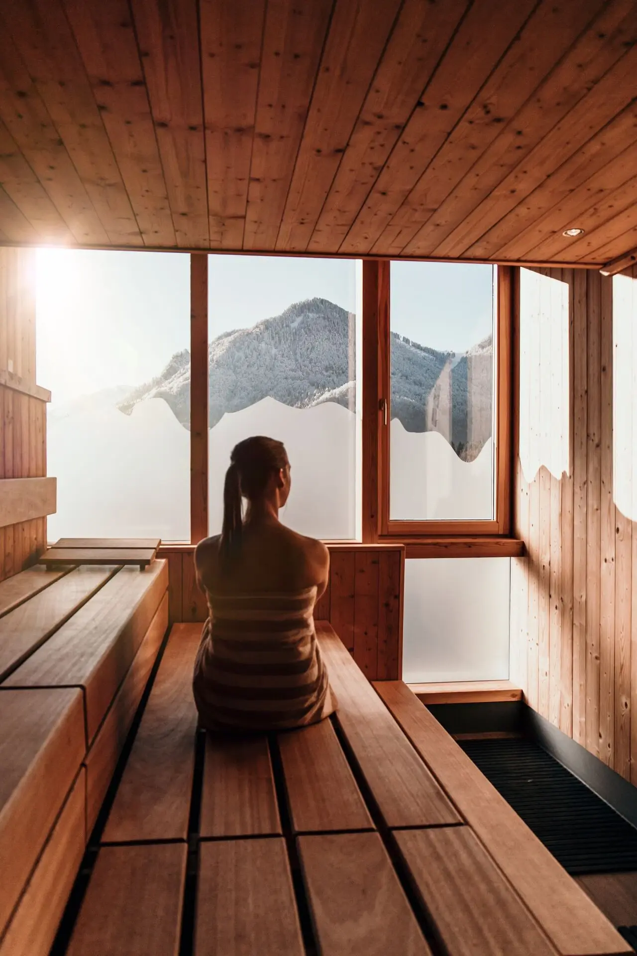 Frau sitzt in einer holzverkleideten Sauna mit Fensterblick auf den Himmel.