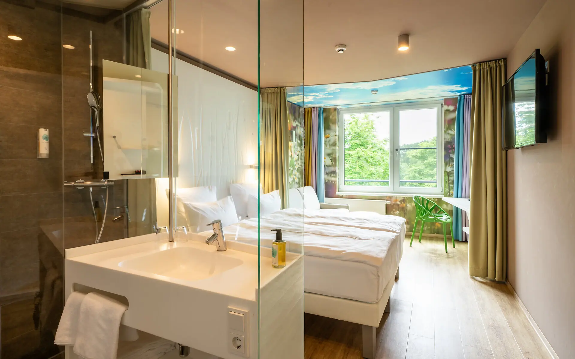 Ein Barriere freies Zimmer mit Naturtapete, Doppelbett und großem Fenster, sowie barrierefreiem Badezimmer mit Dusche. 