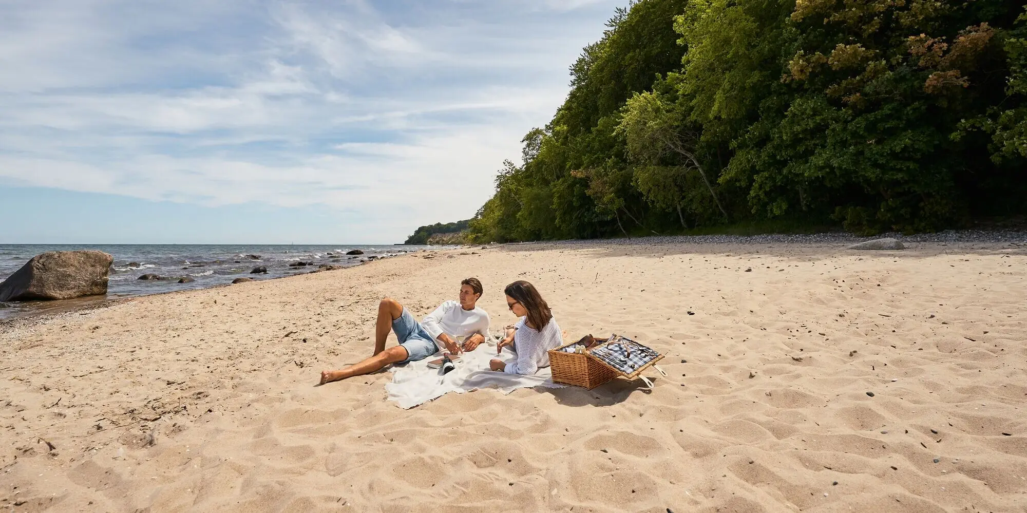 Ein Mann und eine Frau liegen auf einer hellen Decke am Strand von Rügen.