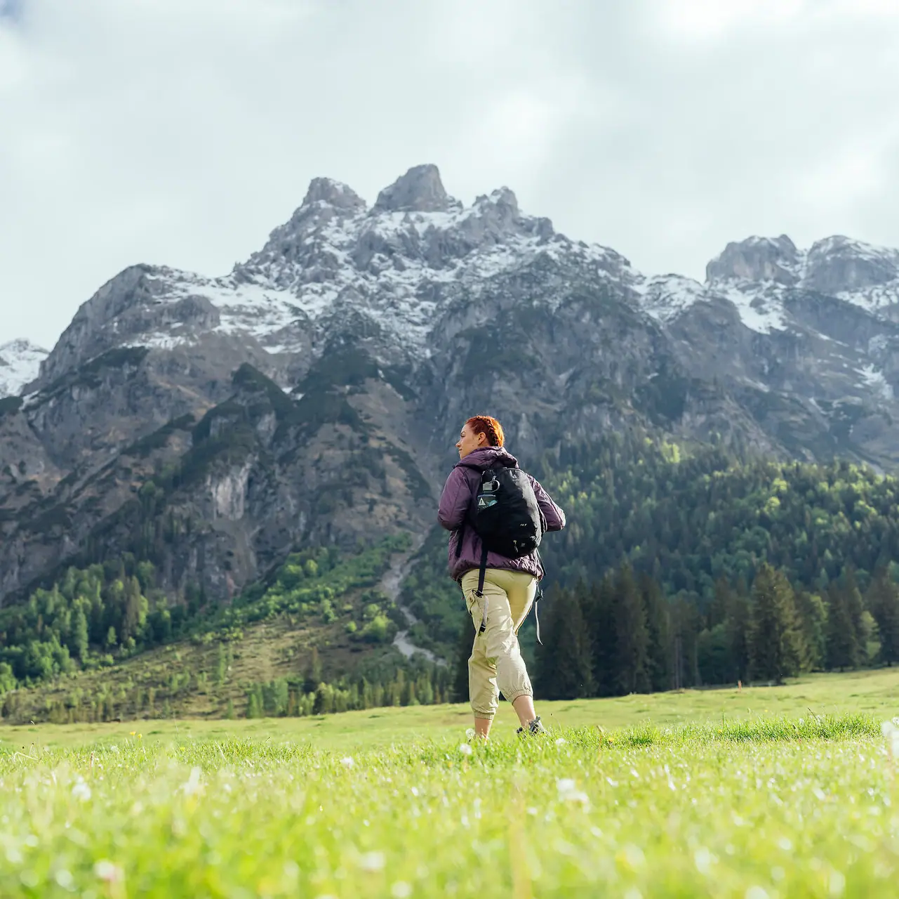 Eine Frau steht in einem Feld mit Bergen im Hintergrund.
