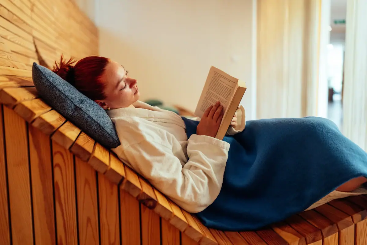 Eine Frau liegt auf einer Holzbank und liest ein Buch.
