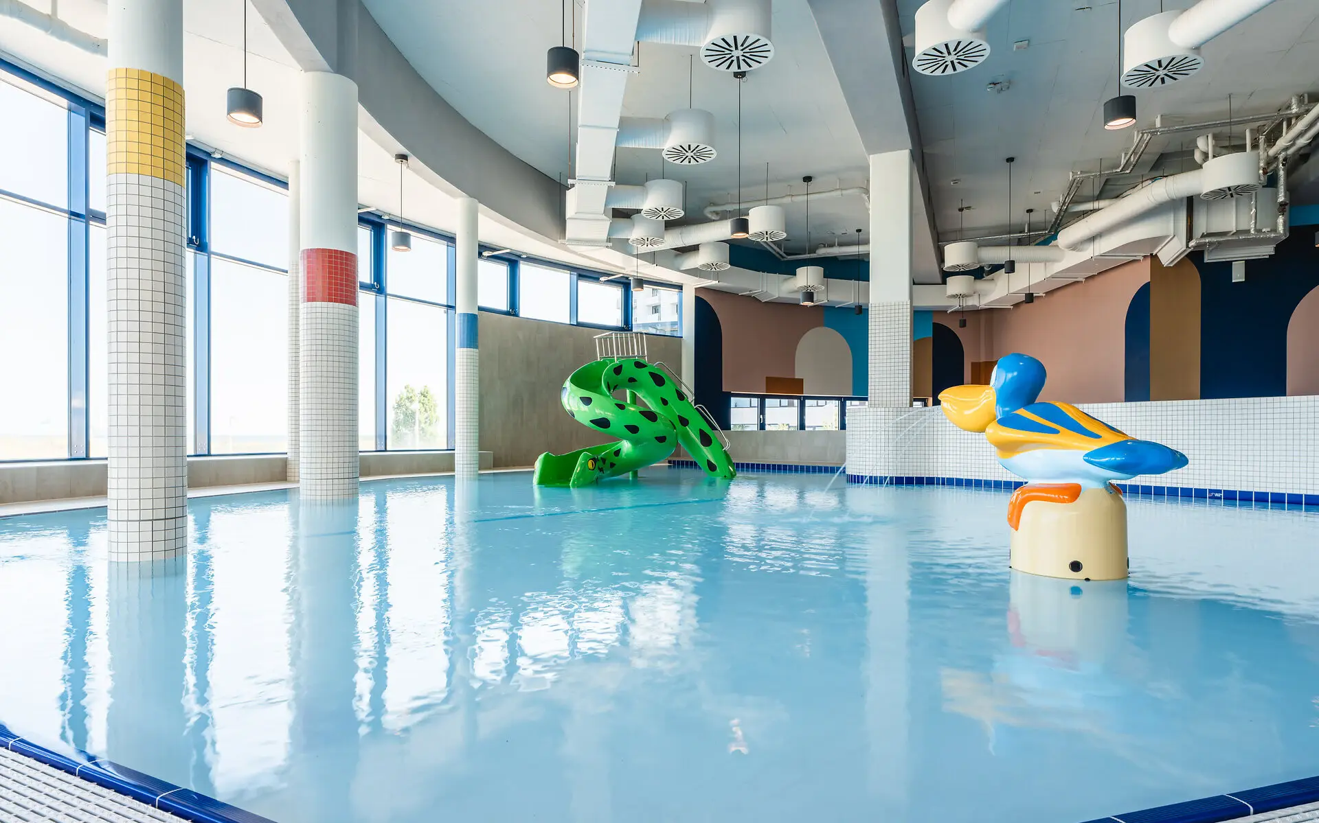 Large indoor swimming pool with a water slide and vibrant blue water.