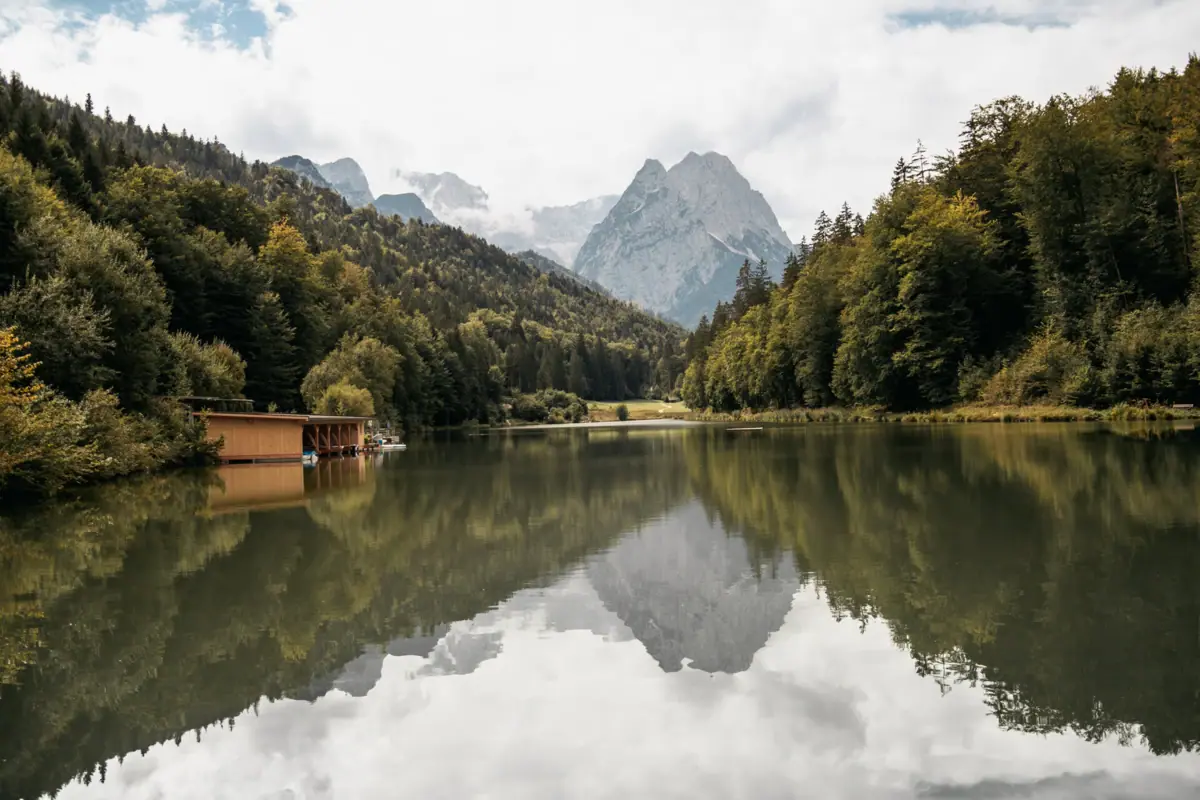 Ein See mit einer Hütte und Bergen im Hintergrund.
