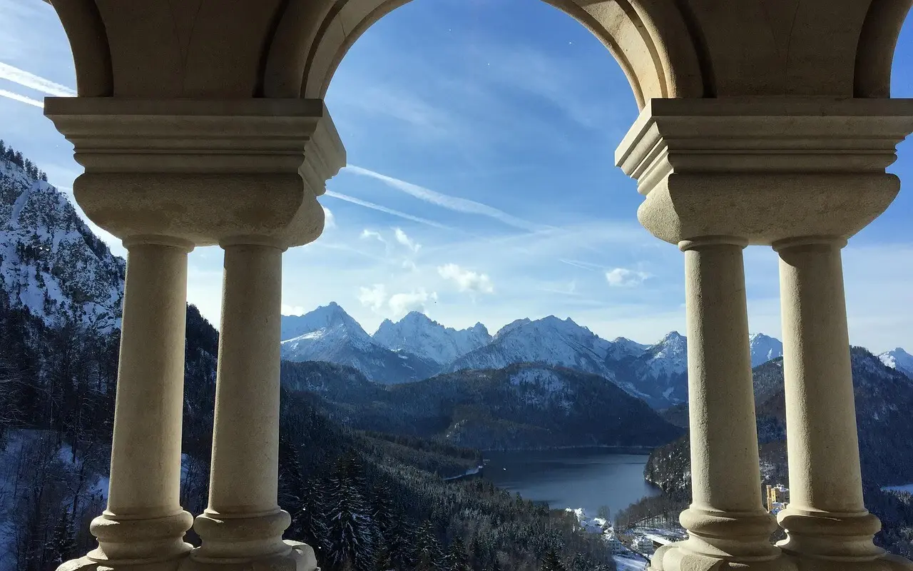 Ausblick vom Schloss Neuschwanstein durch einen Steinbogen mit Blick auf Berge und einen See.